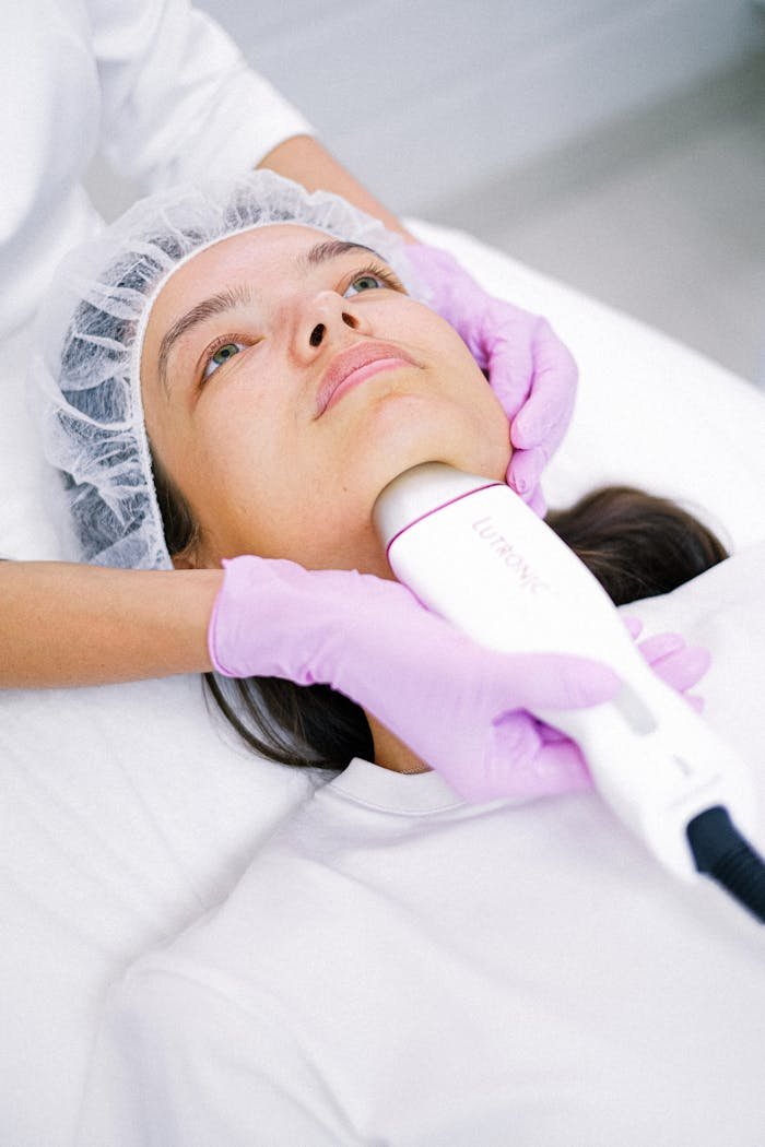 A cosmetologist performs a facial laser treatment on a young woman.