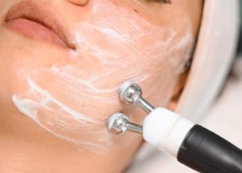 Close-up of a woman getting a facial treatment with a massager and face cream in a spa setting.