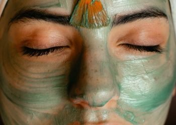 Close-up of a woman enjoying a green cosmetic facial mask application at a spa.